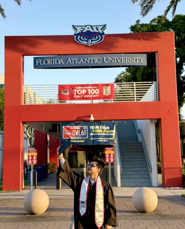 Naim Bin Hasan in cap and gown at the Florida Atlantic University gateway, graduating with an MA in Sociology.